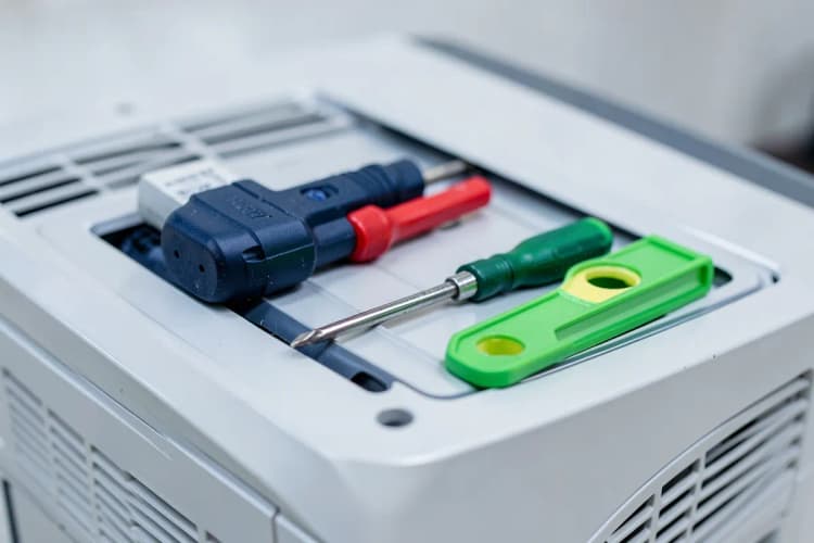 Ferramentas como furadeira, chave de fenda e nível sobre uma caixa de ar-condicionado recém-aberta.